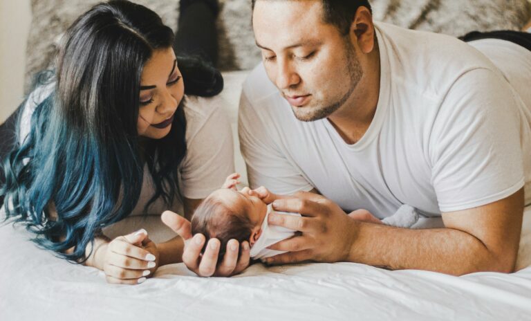 mother and father laying with newborn on bed