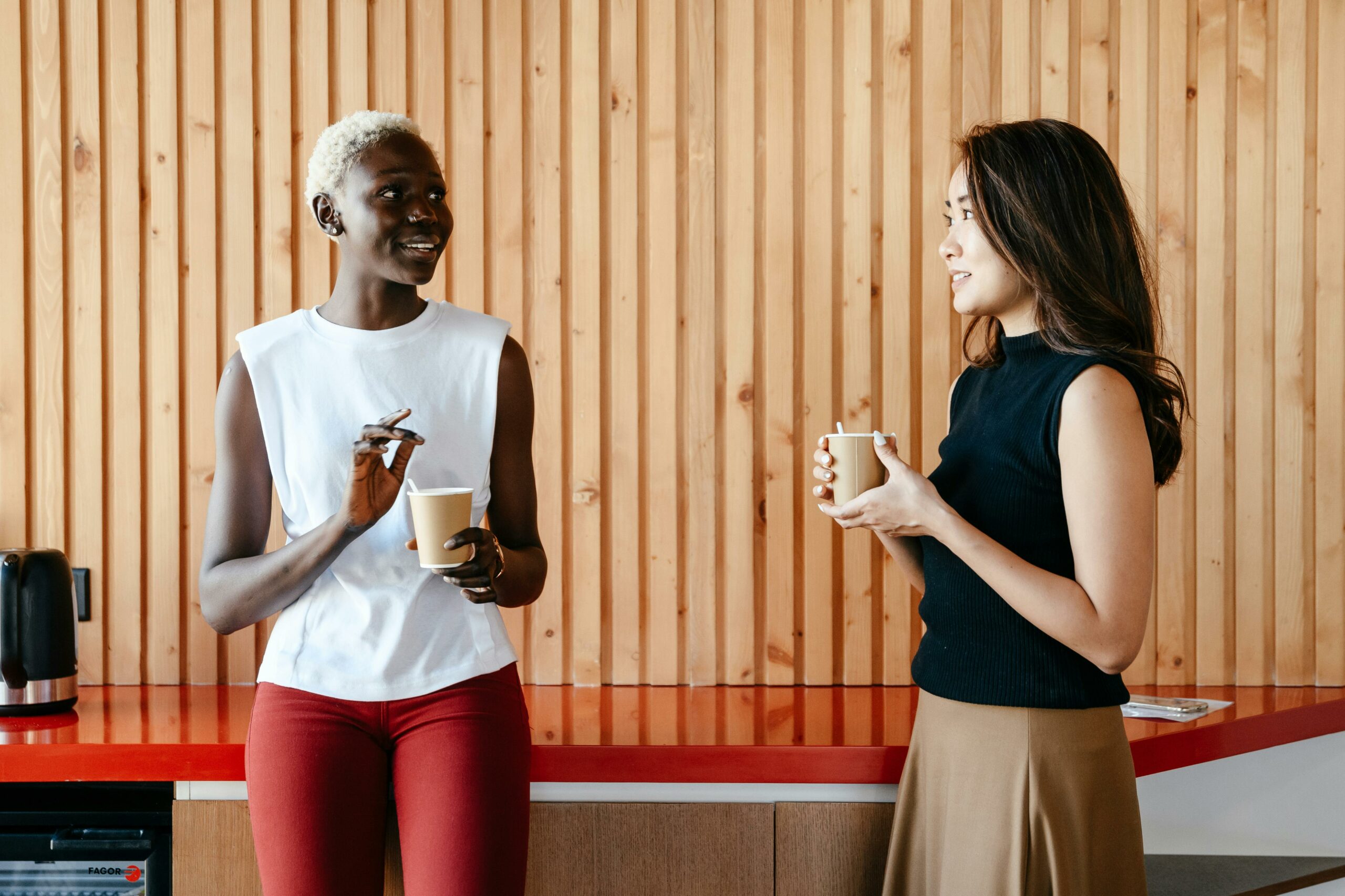 two women holding beverages talking and smiling